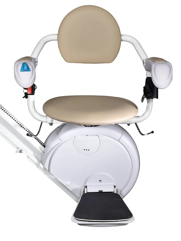 Front view of a Savaria K2 stairlift with the optional V seat, featuring a beige padded seat and open-back design, white armrests with integrated controls, a white carriage housing, and a black foldable footrest mounted on a straight stairlift rail. The V seat design provides additional seating space and improved comfort for some users.