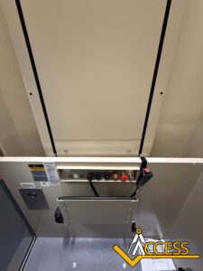 View of an elevator control panel with buttons, a speaker, emergency phone, and handrail. The “Access” logo is visible in the lower right corner. The image is taken from inside the elevator cab.