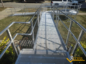 A metal wheelchair ramp with railings extends from a doorway across a lawn to the sidewalk. The ACCESS company logo is visible in the bottom right corner.
