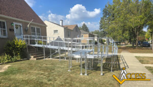 A long, silver wheelchair ramp with railings leads from a house porch to the sidewalk on a lawn, ensuring accessible entry. The ACCESS company logo is in the lower right corner.