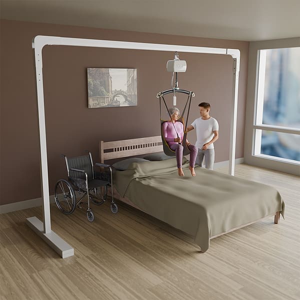 A caregiver uses the SteadyTrack Patient Lift System by Mackworth above a bed in a bright room to assist an elderly person, with a wheelchair close by. A caregiver uses the SteadyTrack Patient Lift System by Mackworth above a bed in a bright room to assist an elderly person, with a wheelchair close by.