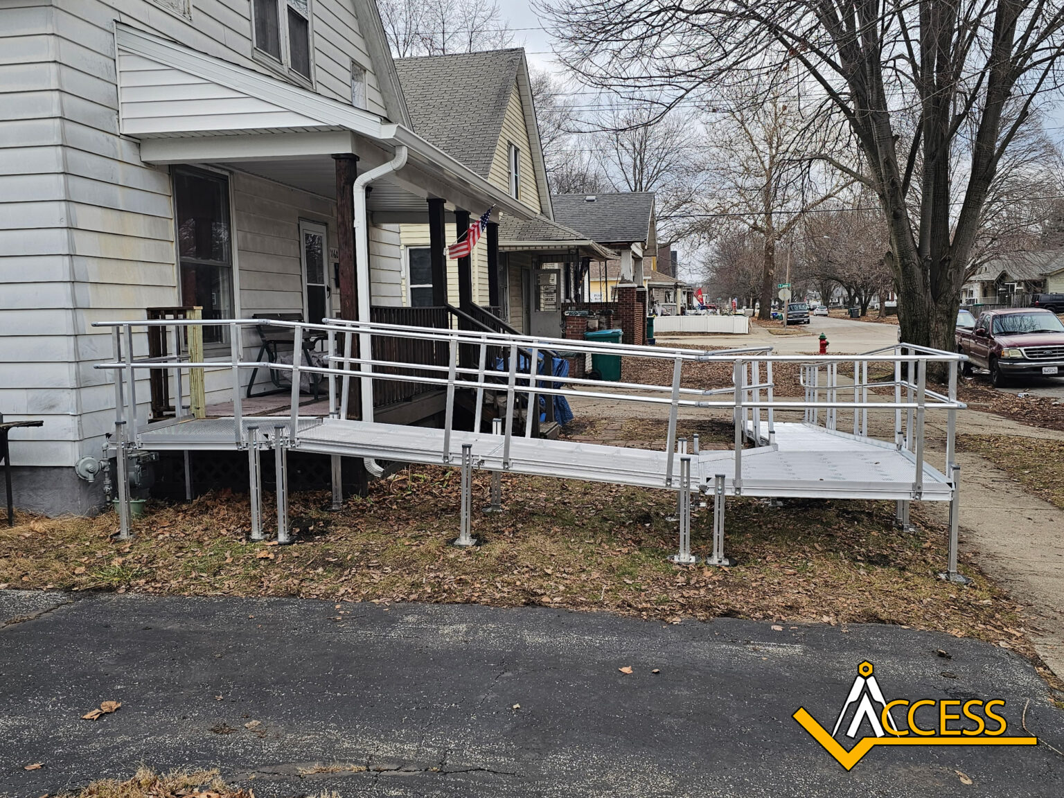 A metal wheelchair ramp with railings leads from a driveway up to the ...