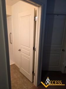 A partially open white bathroom door reveals a tiled floor and a shower with a grab bar; another closed door and a hallway are visible. The Access logo is in the bottom right corner.