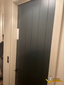 A dark gray paneled door with a black handle is partially closed in a white hallway. Part of a person is visible on the left. The Access logo is in the bottom right corner of the image.