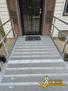 Metal wheelchair ramp with handrails leading to a front door with a screen and storm door. A welcome mat is in front of the door. The Access logo is at the bottom right of the image.