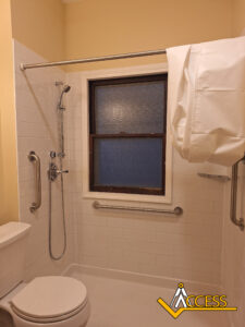 Accessible bathroom with grab bars, a handheld showerhead, a shower curtain partially open, a toilet, and a window with frosted glass. The ACCESS logo is in the bottom right corner.
