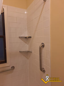A tiled shower corner with two metal grab bars, two corner shelves, and a window on the left. The ACCESS logo is in the bottom-right corner.