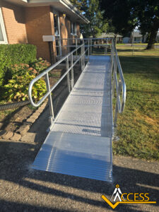 A metal wheelchair ramp with handrails leads from a sidewalk to the entrance of a brick building. The ACCESS company logo is visible in the bottom right corner.