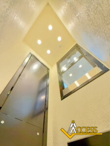 A low-angle view inside an elevator shaft with a black elevator door, a window on the right wall, bright ceiling lights, and the yellow and black Access logo in the bottom right corner.