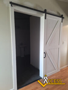 A white sliding barn door is partially open, revealing a small room with a pedestal sink inside. The floor is a mix of light wood and dark tile. The word ACCESS is overlaid in the lower right corner.