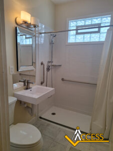 Accessible bathroom with a wall-mounted sink, a toilet, a roll-in shower with grab bars, a handheld showerhead, a shower curtain, a mirror, and a window above the shower. ACCESS logo is in the bottom right corner.