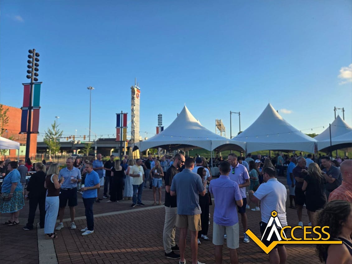 A crowd of people socializes outdoors on a sunny day at the VGM Heartland Conference, with white event tents and city street decorations in the background. The ACCESS logo is visible in the lower right corner, highlighting industry leadership and innovation.