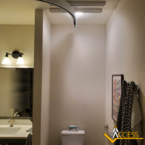 A bathroom with a mirror, sink, and wall light on the left, a toilet in the center, towels on the right wall, and a framed picture above them. The ACCESS logo is in the bottom right corner.