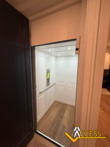A modern residential elevator with white paneled walls, wood flooring, and ceiling lights is open. The Access company logo is visible in the bottom right corner.