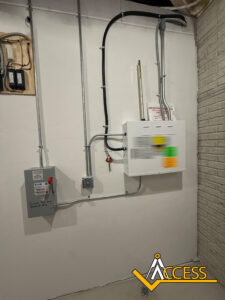 A white wall features mounted electrical panels with various wires connected, including a gray box labeled “Elevator Manual Pit” and a larger white box. The Access company logo is visible in the lower right corner.