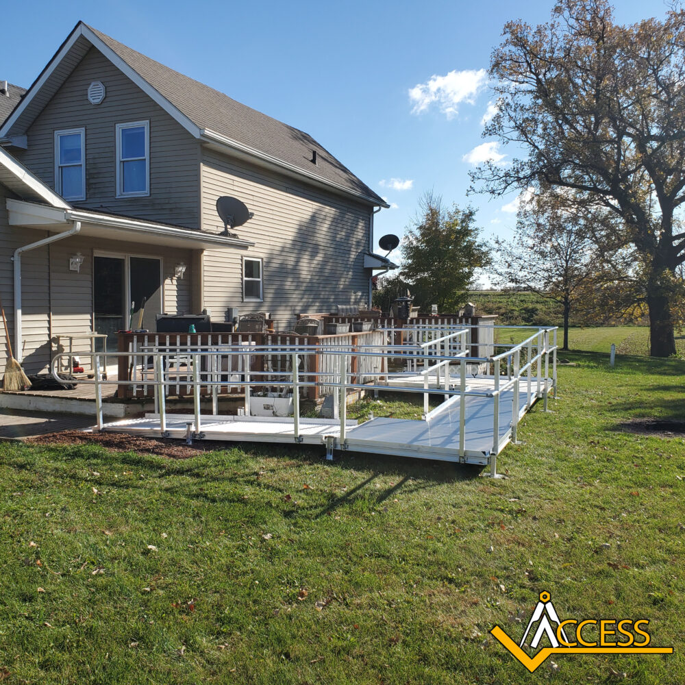 A white wheelchair ramp leads from a grassy yard up to the back porch ...