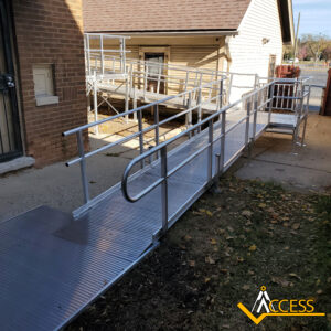 A metal wheelchair ramp with handrails leads to the entrance of a brick building. The ramp has a gentle slope and switchbacks, with the Access company logo in the bottom right corner.
