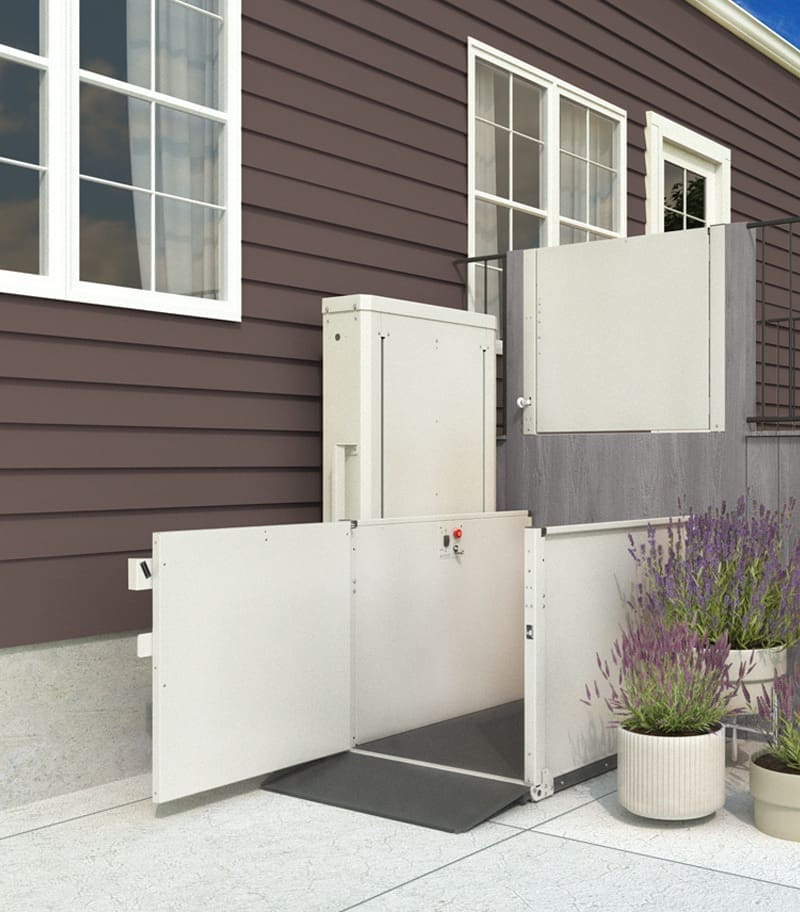 A VPL - 3100/3200 Series - Vertical Platform Lift by Bruno is installed outside a brown house near stairs and potted plants, providing reliable access to an elevated doorway.