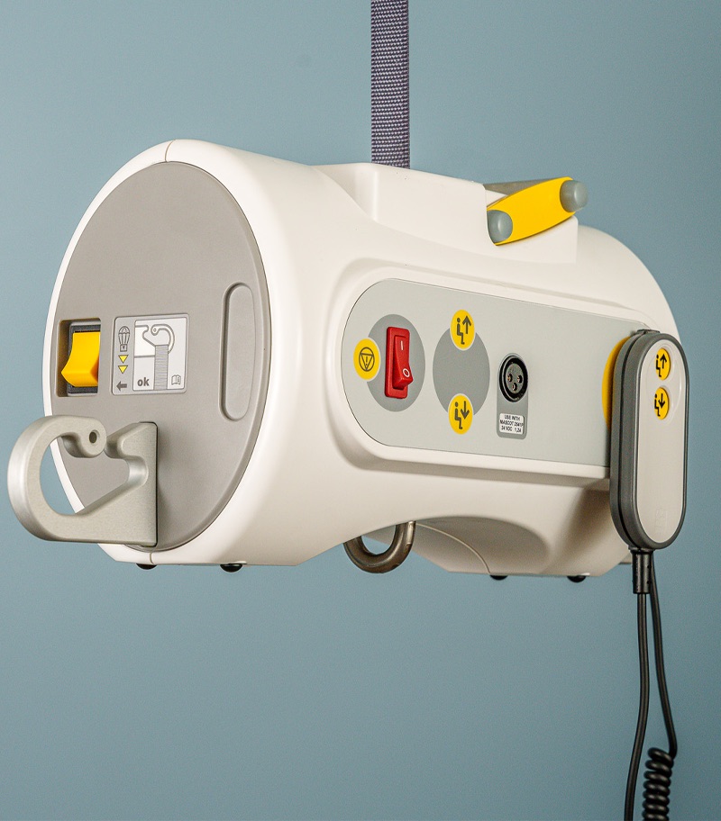 surehands-portable-motor-DSC9401-2840 Close-up of the SureHands portable ceiling lift motor featuring integrated controls, emergency stop button, carrying handle, and handheld remote for safe and convenient patient transfers.