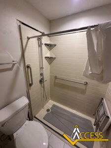 Accessible bathroom remodel in Mattoon, Illinois featuring a low-threshold walk-in shower with white subway tile, stainless steel grab bars, a handheld showerhead, corner shelving, a fold-down shower seat, and a non-slip shower mat designed to improve safety and accessibility.