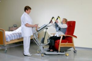 SureHands mobile patient 1620 with a caregiver helping a patient into a chair sitting.