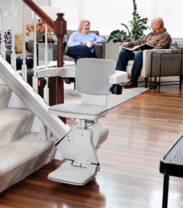 Bruno Elan SRE-5000 straight stair lift installed on a carpeted staircase in a residential home, featuring a padded seat, folding footrest, and slim rail design for safe, reliable home accessibility.