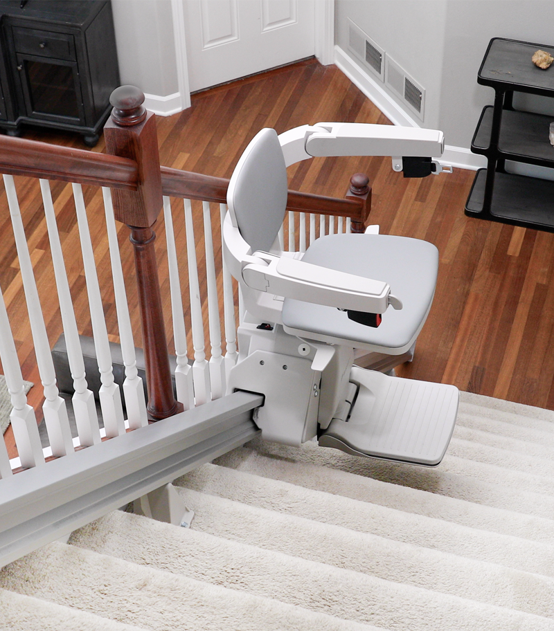 bruno-elan-5000-on-stairs-qrter-way-up Bruno Elan SRE-5000 straight stair lift traveling on a carpeted residential staircase, featuring a padded seat, folding armrests, folding footrest, and compact rail system for safe, dependable home accessibility.