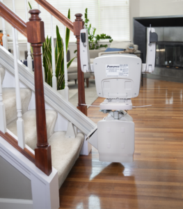 Rear view of a folded Bruno Elan SRE-5000 straight stair lift parked at the bottom of a carpeted residential staircase, showcasing its space-saving design and compact rail system.