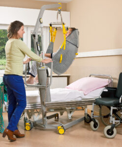 Caregiver helping patient into bed using a mobile patient lift 1640 in a sling.