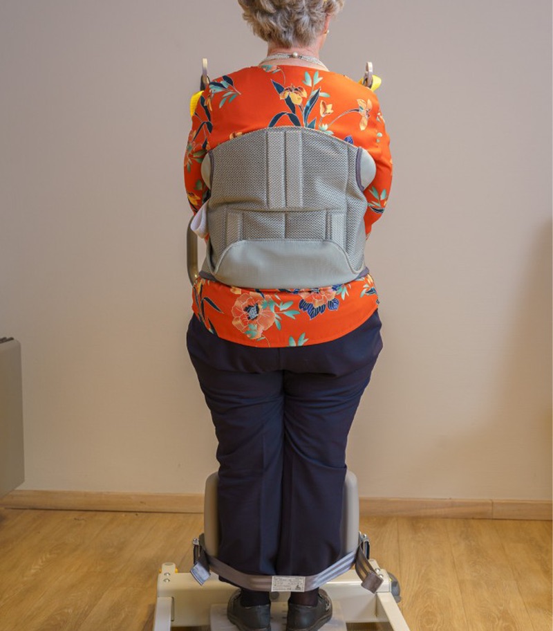 surehands-mobile-patient-lift-2620-03 Rear view of a patient using the SureHands Stand Assist 2620 with a supportive standing sling secured around the torso, demonstrating proper positioning for safe sit-to-stand transfers and assisted mobility.