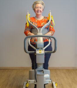 Front view of a patient using the SureHands Stand Assist 2620 with a supportive standing sling, demonstrating safe sit-to-stand positioning while securely supported by the powered patient lift.