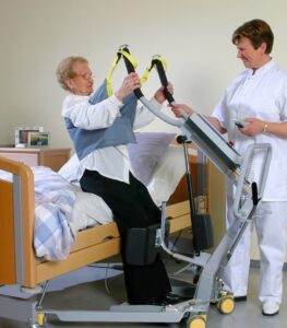 SureHands stand assist 1620 with a caregiver helping a patient into bed using a sling.