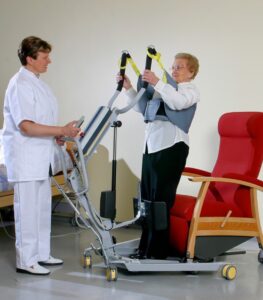 SureHands stand assist 1620 with a caregiver helping a patient into a chair using a sling.