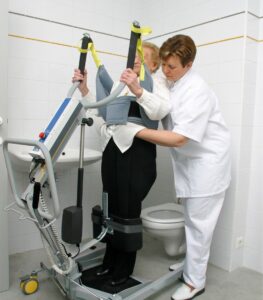 SureHands stand assist 1620 with a caregiver helping a patient onto a toilet using a sling.