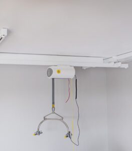SureHands Traverse Rail ceiling lift system with motor unit and sling hanger mounted on parallel overhead rails for full-room patient transfers.