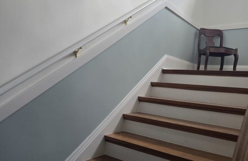 White stairlift rail installed along a short residential staircase with dark wood steps, white trim, and light gray walls, demonstrating a compact accessibility solution for navigating changes in floor level.