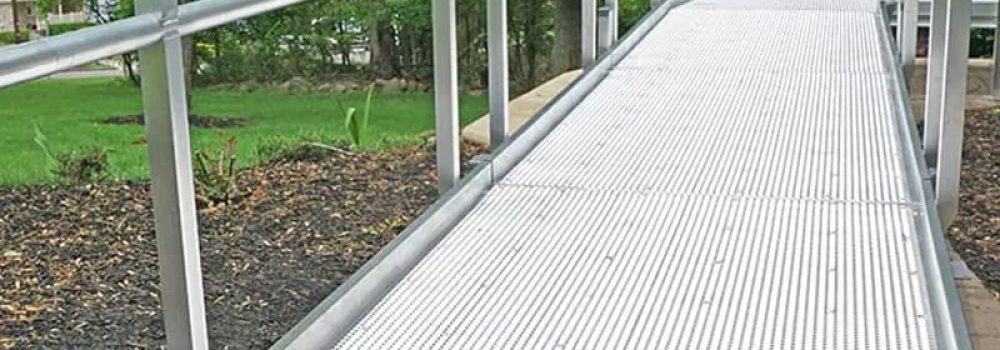 Residential wheelchair ramp with mesh decking to prevent snow accumulation on surface and with lush forestry in background